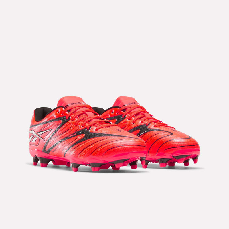 A pair of Reebok Sidewinder 26 League Firm Ground Cleats for big kids in bright red, with black and silver accents and firm ground studs on the soles, displayed against a plain white background.