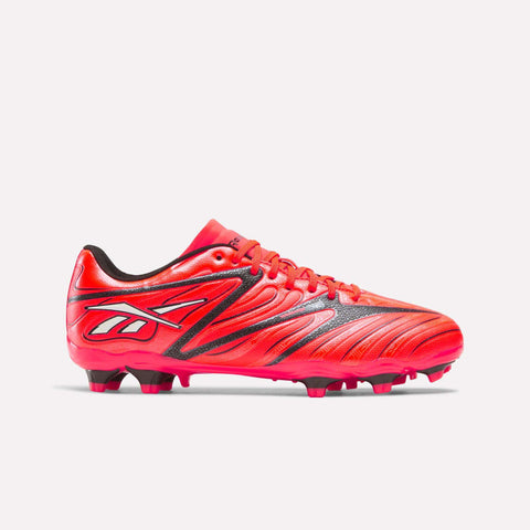 The Reebok Sidewinder 26 League Firm Ground Cleats for Big Kids are shown in Neon Cherry and Rival Red with black accents, featuring a stylized logo on the heel, a textured surface, and red firm ground studs on the sole, all displayed against a plain white background.
