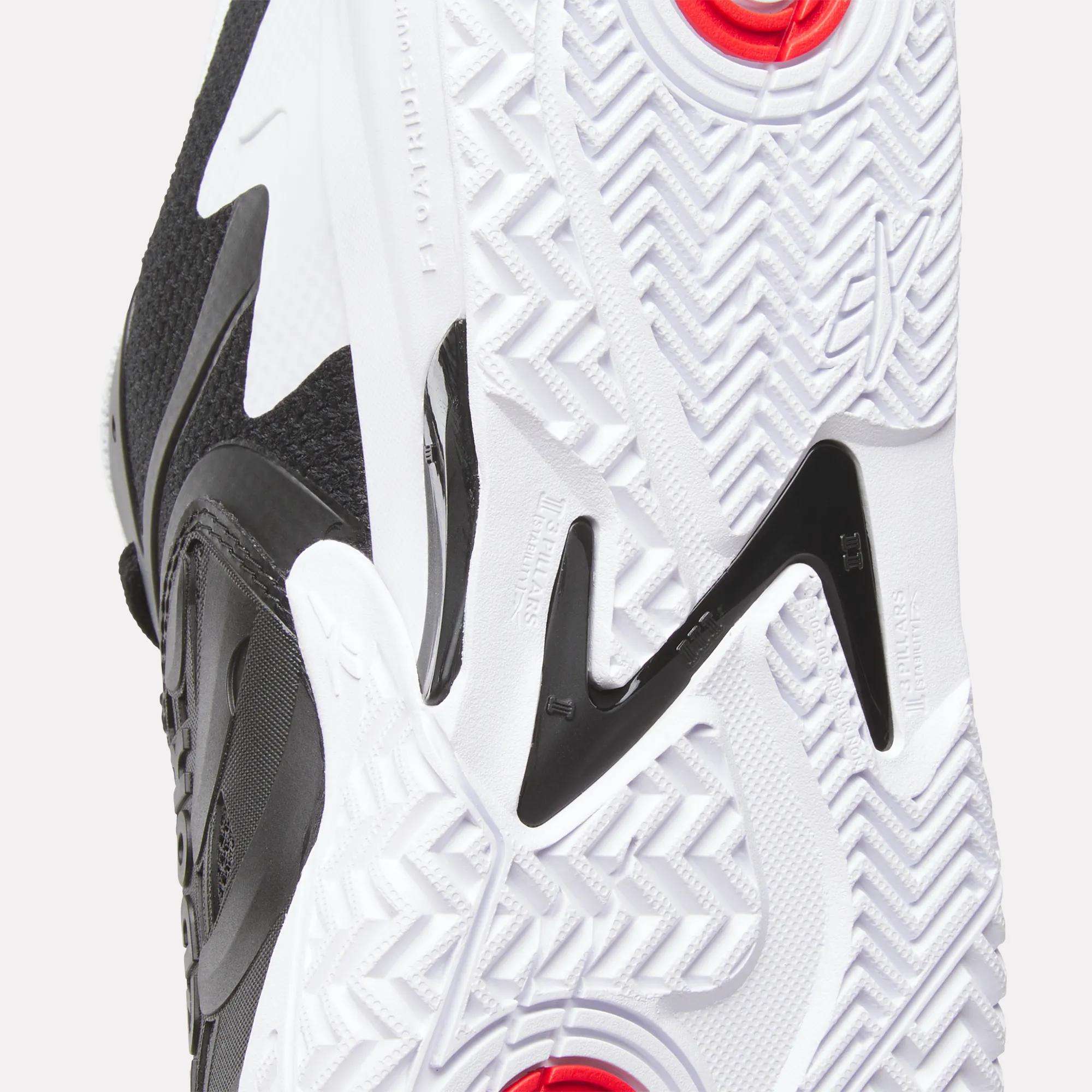 Close-up of the sole on Reebok Phase EVO Tennis Shoes, featuring a white and black geometric tread with red circular accents and textured details for enhanced grip and responsive rebound.