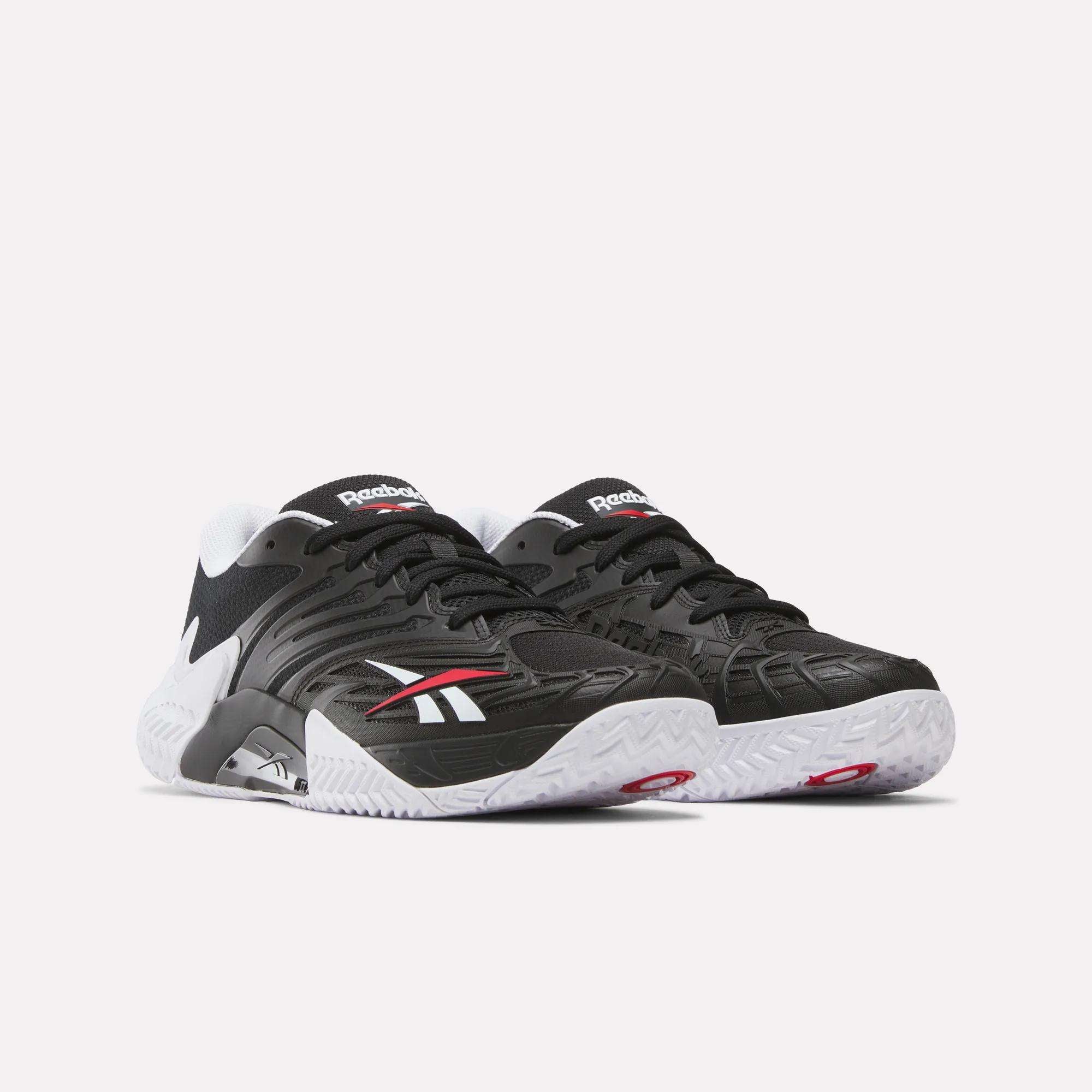 The Reebok Phase EVO Tennis Shoes feature a black finish with white soles, white and red accents, and the Reebok logo on the sides. They offer responsive rebound and are displayed against a plain light background.