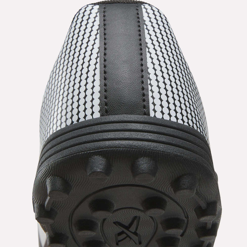 Close-up view of the heel and sole of the Reebok Strike Turf Soccer Shoes, showcasing textured rubber studs, a central black stripe, and a white upper patterned with small black circles—ideal as practice soccer shoes.