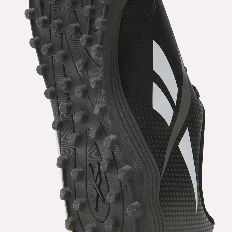 Close-up of the sole of a black Reebok Strike Turf Soccer Shoe, highlighting its rubber traction studs and white geometric Reebok logos on the side—ideal for soccer practice.