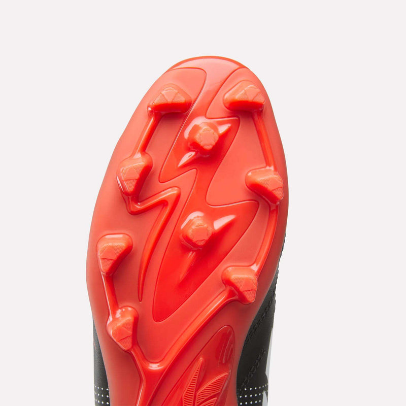 Close-up of the red sole of Reebok Strike Multi-Ground Soccer Shoes - Big Kids, featuring six angular studs and a textured turf pattern, set against a white background.