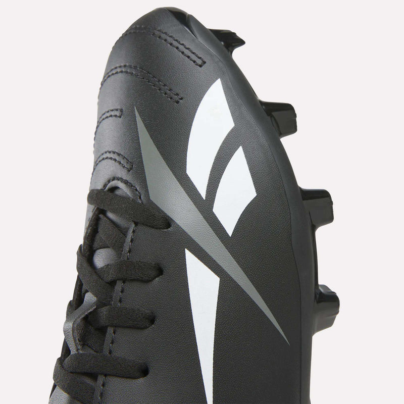 A close-up of the Reebok Strike Multi-Ground Soccer Shoes for Big Kids, featuring black uppers with white and silver geometric designs, black laces, and plastic studs on the outsole—perfect for use on turf.