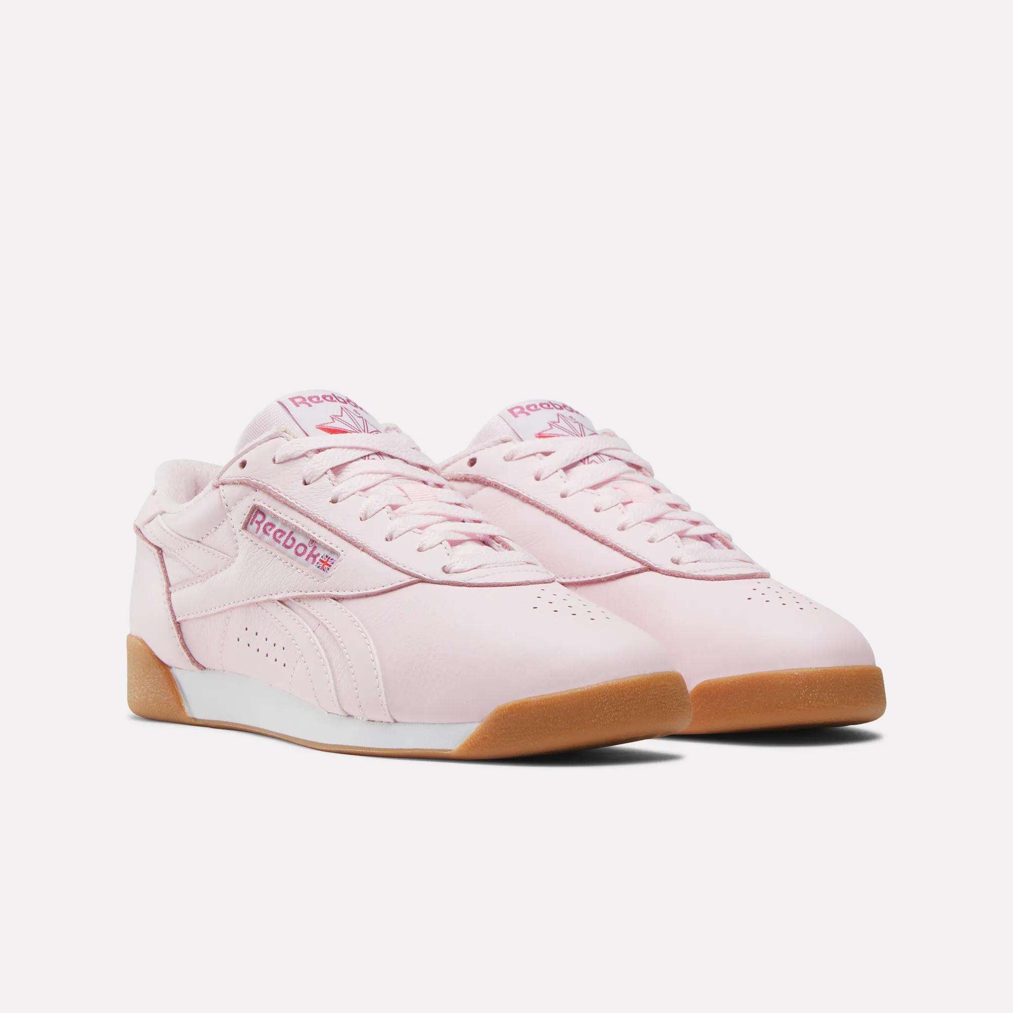 A pair of Reebok Women's Freestyle Lo Shoes in light pink with gum rubber soles and matching laces, featuring the pink Reebok logo on the side and tongue, perfect for daily wear, shown on a plain white background.