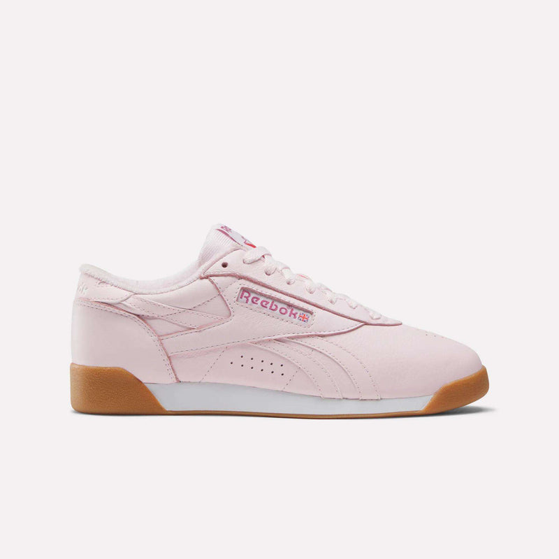 The Reebok Women's Freestyle Lo Shoes feature a light pink leather upper, white sole, tan gum outsole, pink laces, and the Reebok logo on the side and tongue. Ideal for everyday wear, they stand out against a plain white background.