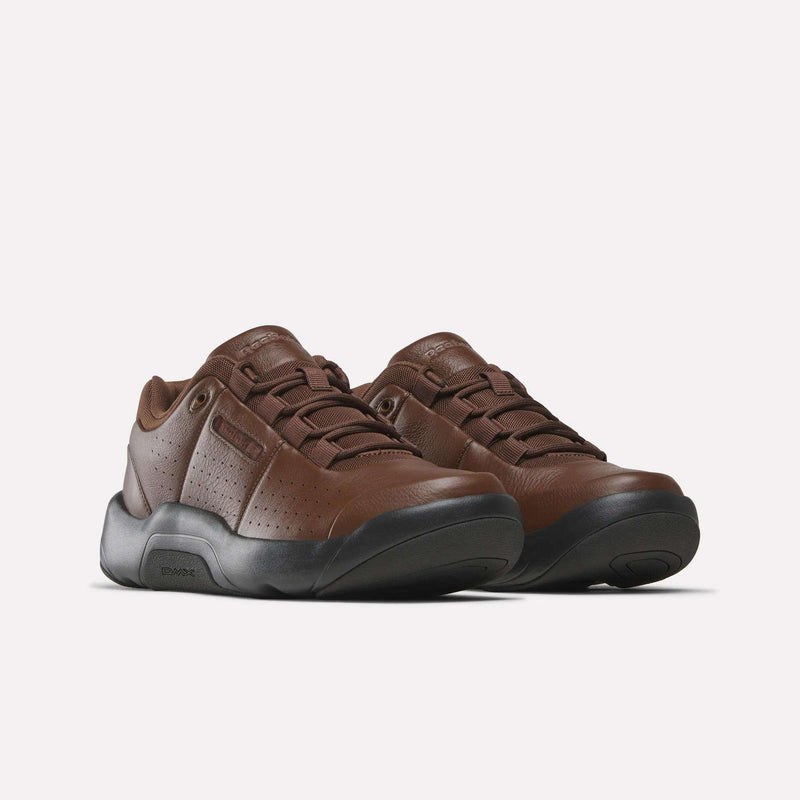 A pair of Reebok DMX Comfort+ Classic sneakers in brown premium leather, featuring black rubber soles, dynamic air cushioning, perforated sides, and brown laces, displayed on a plain white background.