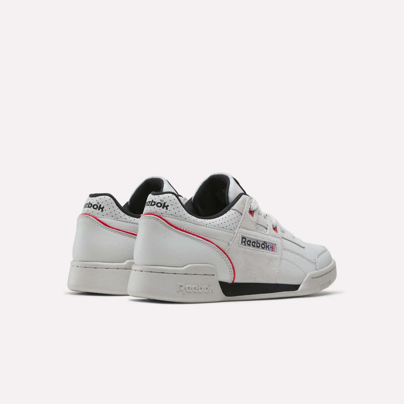 A pair of Reebok Workout Plus Shoes in white, featuring black and pink accents, are displayed against a light background. One shoe is positioned to show the back while the other faces forward, highlighting the Reebok branding and vintage-inspired design details.