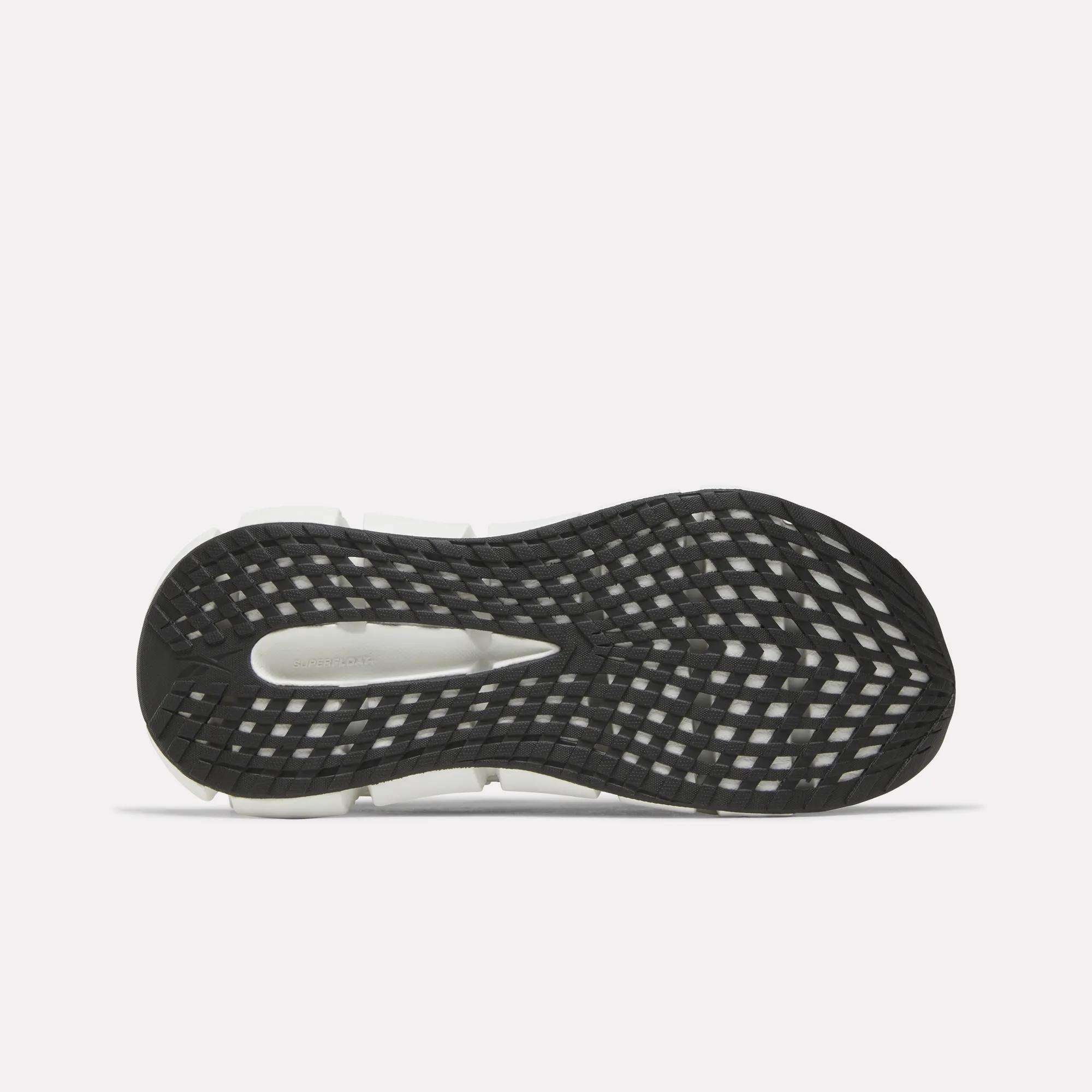 The image displays the black and white sole of Reebok Women's FloatZig 2 Running Shoes, viewed from beneath. The tread has a crisscross grid for traction, and Superfloat+ cushioning provides a springy feel.
