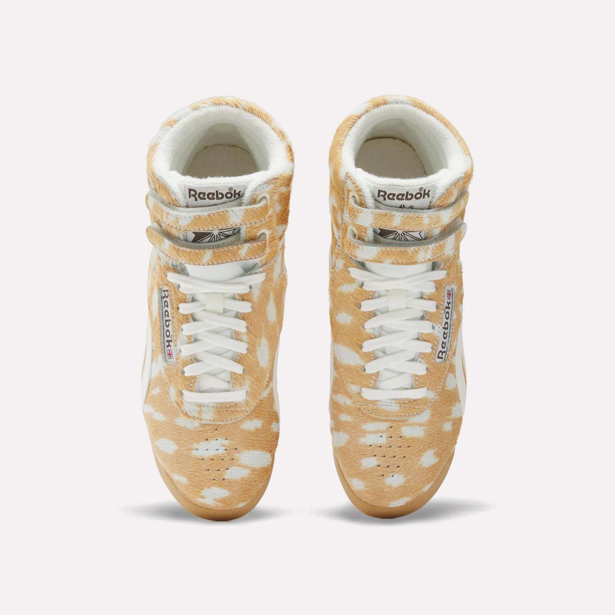 Top view of Women's Freestyle Hi Shoes by Reebok, featuring a classic 80s high-top design with a tan and white spotted fur-like pattern, white laces, and signature Reebok branding on the tongue and side.