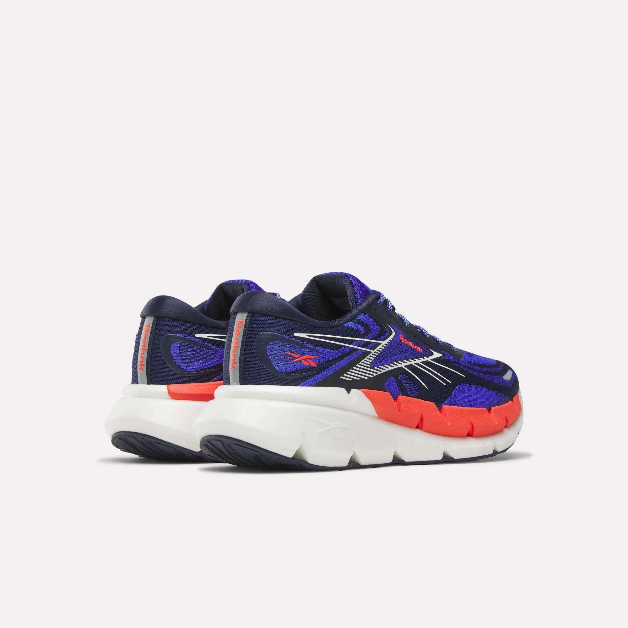 The Reebok Men's FloatZig Double Running Shoes feature navy blue and purple uppers with orange accents, silver detailing, thick white soles, and StableStack construction, shown from the back and side on a light background.