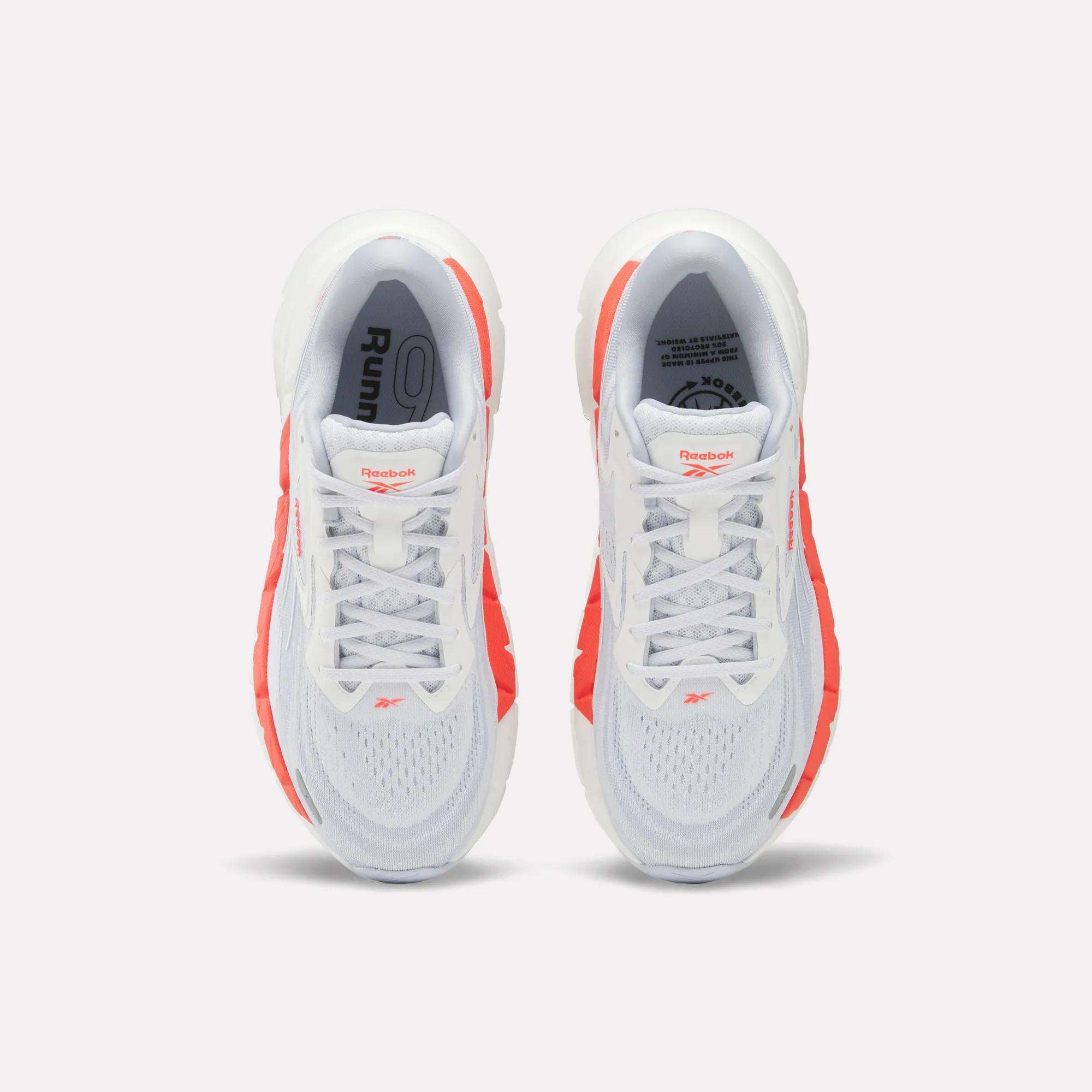 Top view of Women's FloatZig Double Running Shoes by Reebok, in white with bright orange side accents and branded tongue, set against a plain light background.