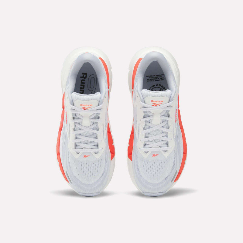 Top view of Women's FloatZig Double Running Shoes by Reebok, in white with bright orange side accents and branded tongue, set against a plain light background.