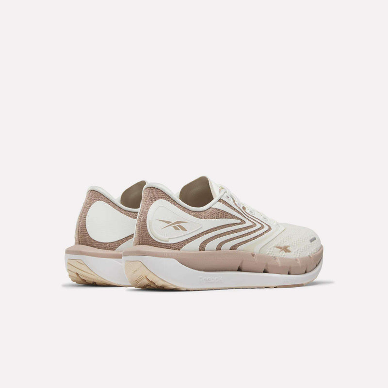 The Women's FloatZig Tread Running Shoes by Reebok feature a low-cut, breathable mesh upper in beige and white with light brown accents and the Reebok logo on the side—ideal for treadmill workouts, shown against a plain white background.