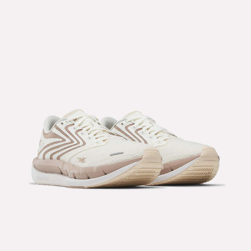 A pair of Reebok Women's FloatZig Tread Running Shoes with beige accents and wavy stripe details, featuring a breathable mesh upper, textured soles, and white laces—perfect for treadmill workouts.