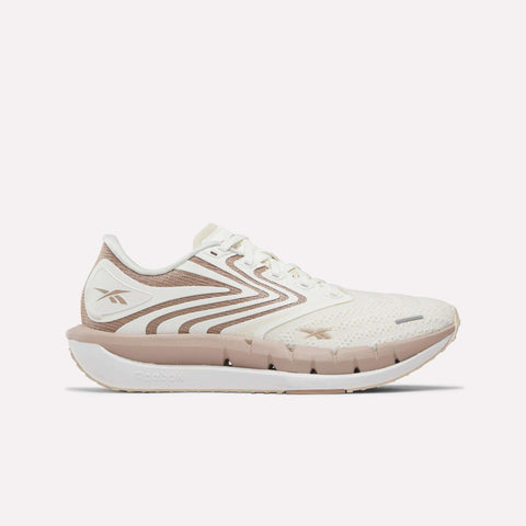 The Reebok Women's FloatZig Tread Running Shoes feature a white mesh upper with light beige accents, geometric side patterns, and a white sole—ideal for treadmill workouts. The Reebok logo appears on the heel and side.