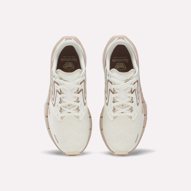 Top view of Reebok Women's FloatZig Tread Running Shoes in white with beige accents and soles, featuring a breathable mesh upper and lace-up design, displayed on a light background.