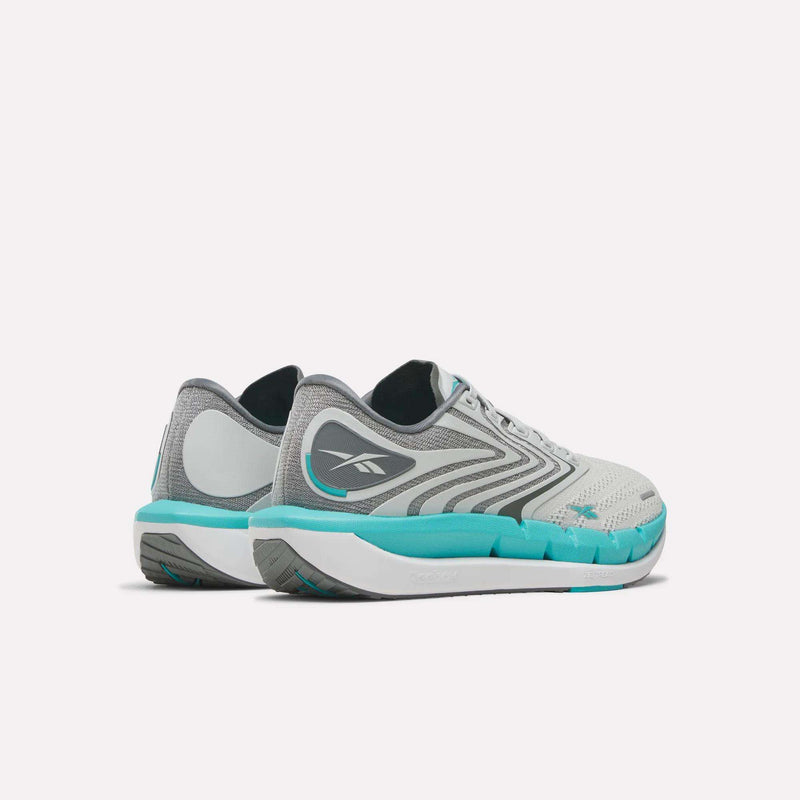 A pair of Reebok Women’s FloatZig Tread Running Shoes in gray and white with teal soles and black logos, designed for treadmill workouts, displayed from a rear side angle on a plain white background.
