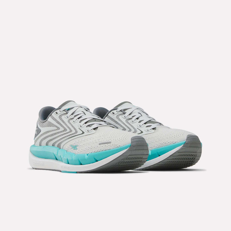 A pair of Reebok Women’s FloatZig Tread Running Shoes in white and gray with teal accents, displayed side by side on a white background. These shoes feature mesh uppers and thick, cushioned soles, making them ideal for treadmill workouts.