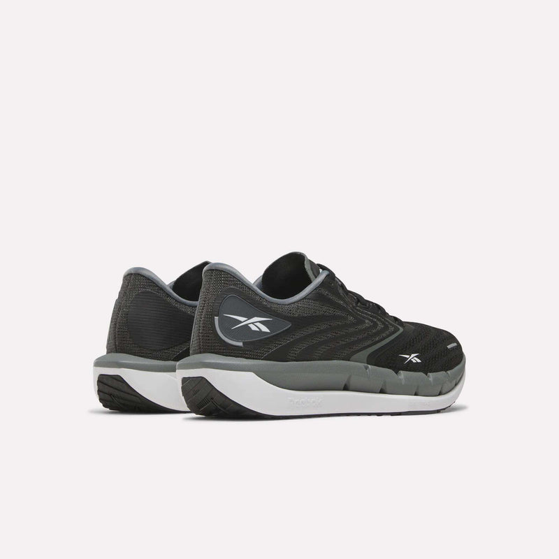 A pair of Reebok Women’s FloatZig Tread Running Shoes in black and gray with white soles, shown from the back and side. These shoes feature a breathable mesh upper and display the Reebok logo on the heel and outer side, making them perfect treadmill running shoes that combine comfort and style.