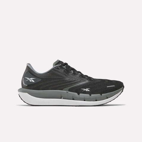 A pair of Reebok Women’s FloatZig Tread Running Shoes in Black/Washed Black/Chalk, featuring a white sole, the Reebok logo on the side and heel, and a breathable mesh upper, is shown from the left against a plain white background.