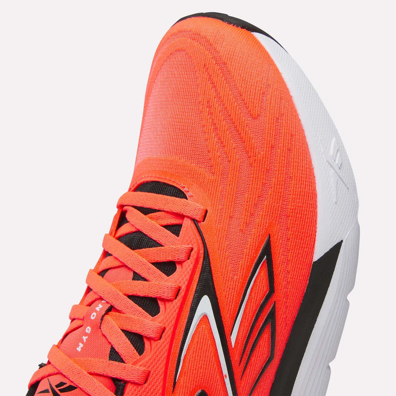Close-up of the front and side of Reebok Nano Gym 2.0 Training Shoes in orange with black and white accents, showing textured details, a black-and-white sole, visible laces, and part of the tongue.