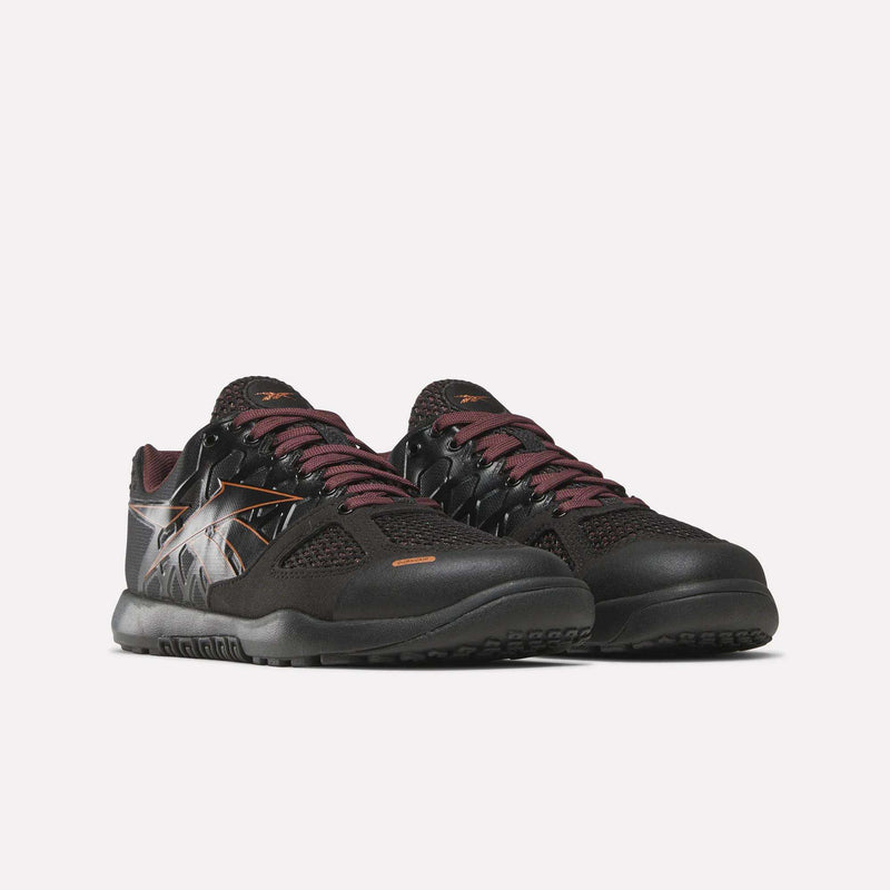The Reebok Women’s Nano 2.0 Training Shoes are black with maroon laces, white and orange accents, and a patterned design on the sides. Displayed on a plain white background, these training shoes are ideal for women’s functional fitness routines.