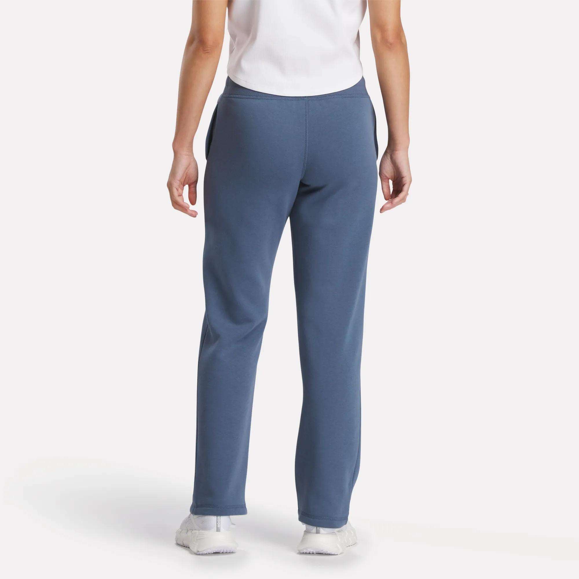 A person wearing a white T-shirt and Reebok Women's Cozy Classic Sweatpants, seen from the back. The soft cotton-blend sweatpants are paired with white sneakers against a plain, light background.