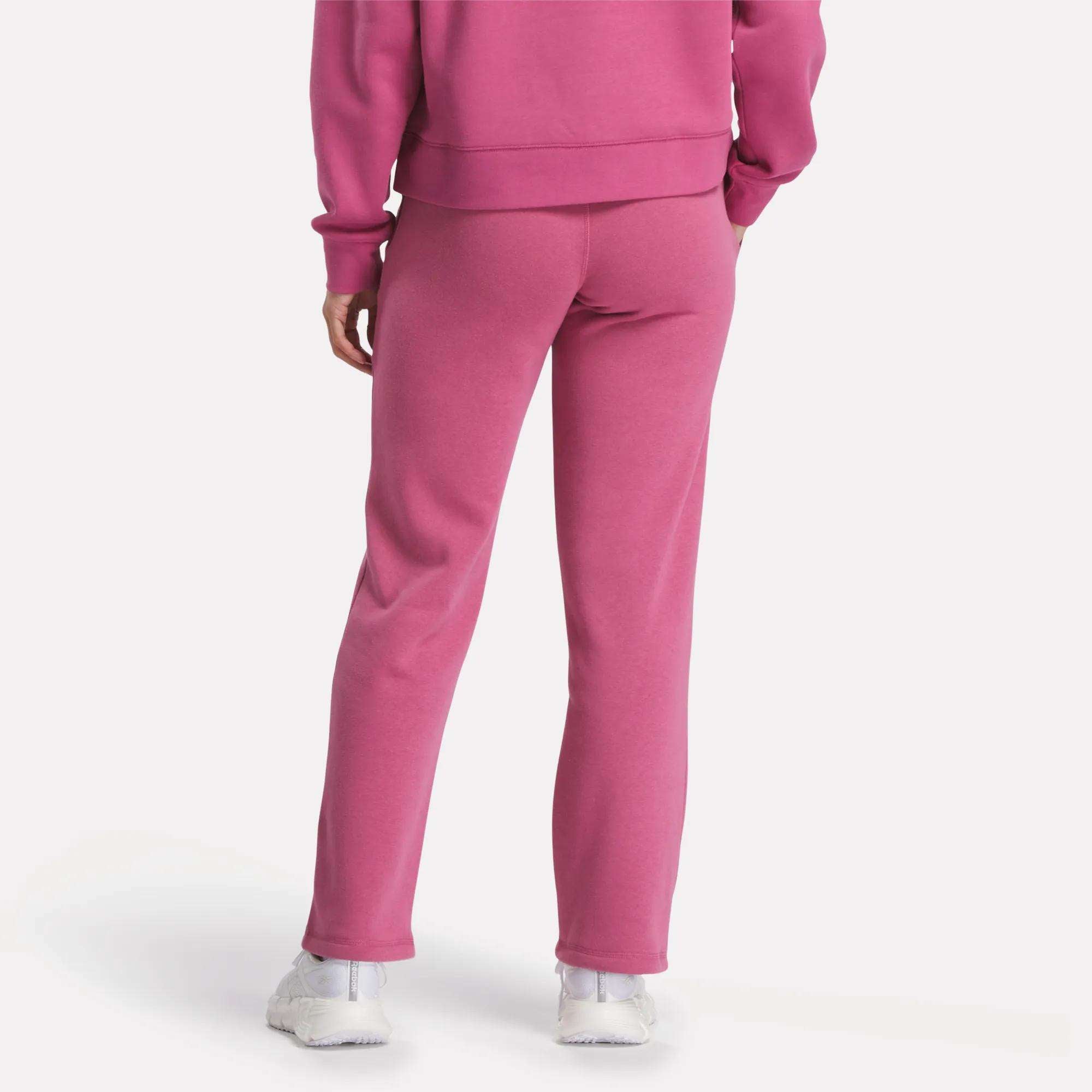 A woman wearing Reebok Women's Cozy Classic Sweatpants in pink, made from a soft cotton blend.