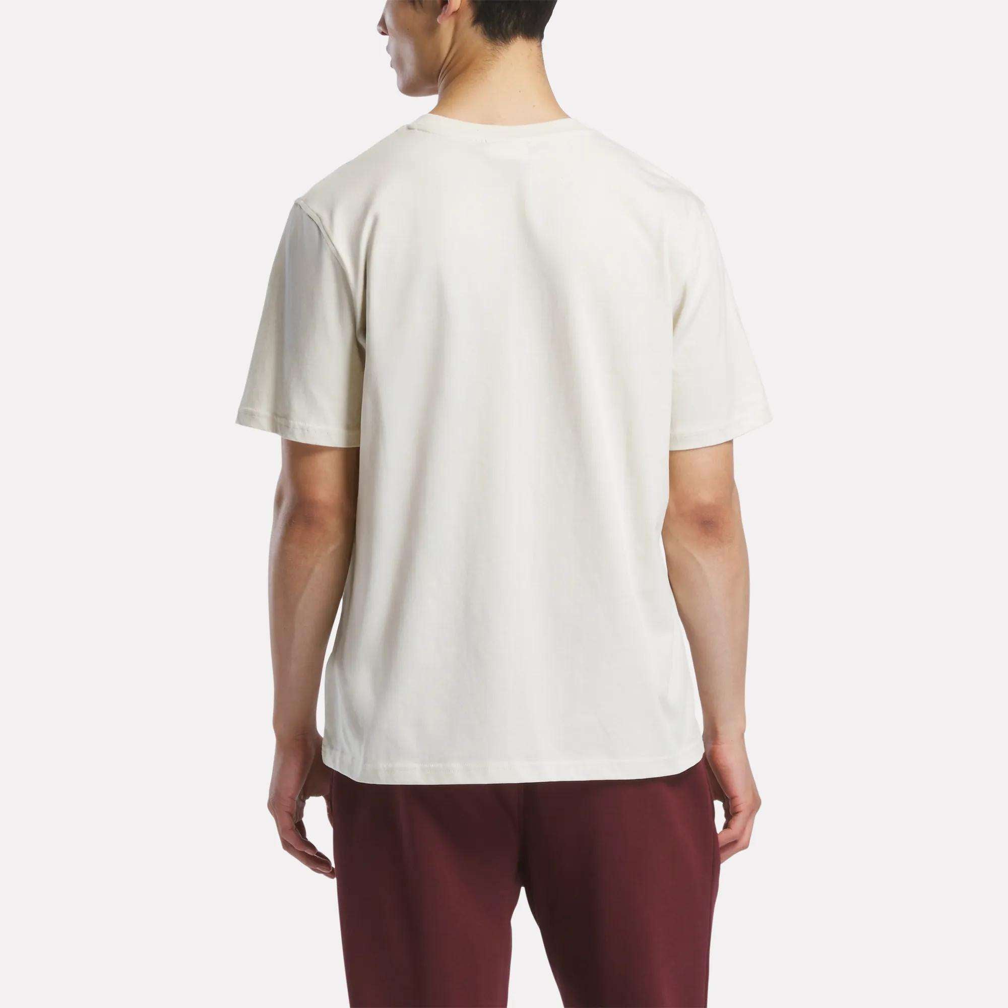 A person faces away from the camera wearing a Reebok Men's Logo Crewneck T-Shirt and maroon pants, standing against a neutral background.