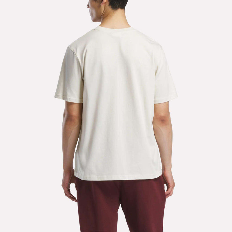 A person faces away from the camera wearing a Reebok Men's Logo Crewneck T-Shirt and maroon pants, standing against a neutral background.