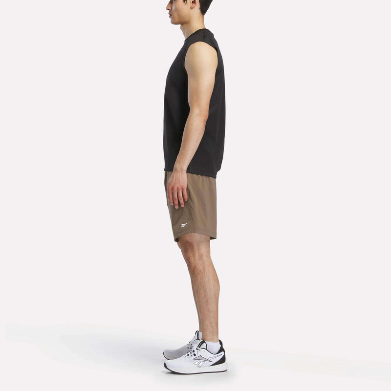 A man in profile wears a black sleeveless shirt, Reebok Men's Woven Shorts, and white athletic shoes against a plain white backdrop.