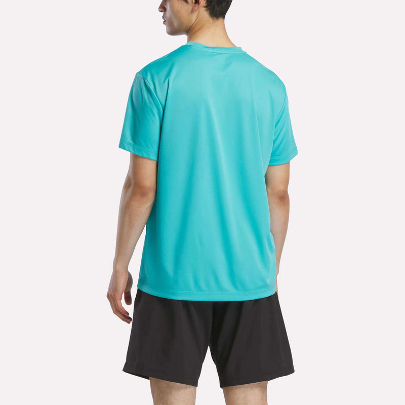 A person stands with their back to the camera, wearing a turquoise Reebok Men's Short Sleeve Tech Training T-Shirt and black shorts against a plain white background.
