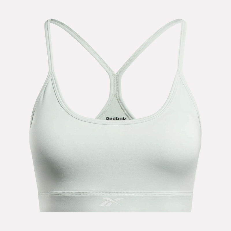 The Reebok Women’s Strappy Sports Bra in light gray features thin straps and a racerback design, shown against a white background. Ideal for medium-impact workouts, this quick-drying sports bra displays the black Reebok logo on the front as well as subtly on the elastic band.