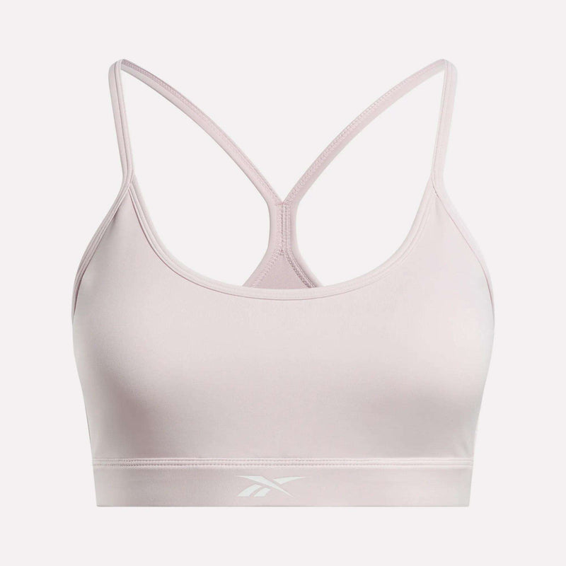 The Women's Strappy Sports Bra by Reebok features a light pink color, thin racerback straps, and a subtle front logo on the band. Made from smooth, stretchy quick-drying fabric, it delivers comfort and support for medium-impact workouts.