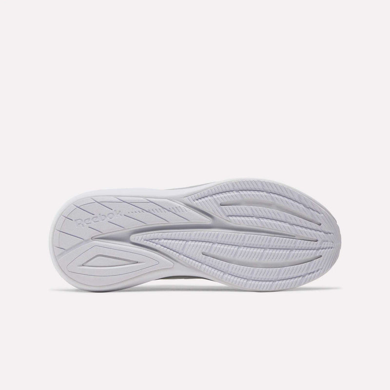 The bottom view of a Women’s Viva Speed Shoe by Reebok, in white, displays a patterned rubber sole with curved and linear grooves for traction. Designed for extra cushioning, these shoes also feature the Reebok logo embossed on the left side of the sole.
