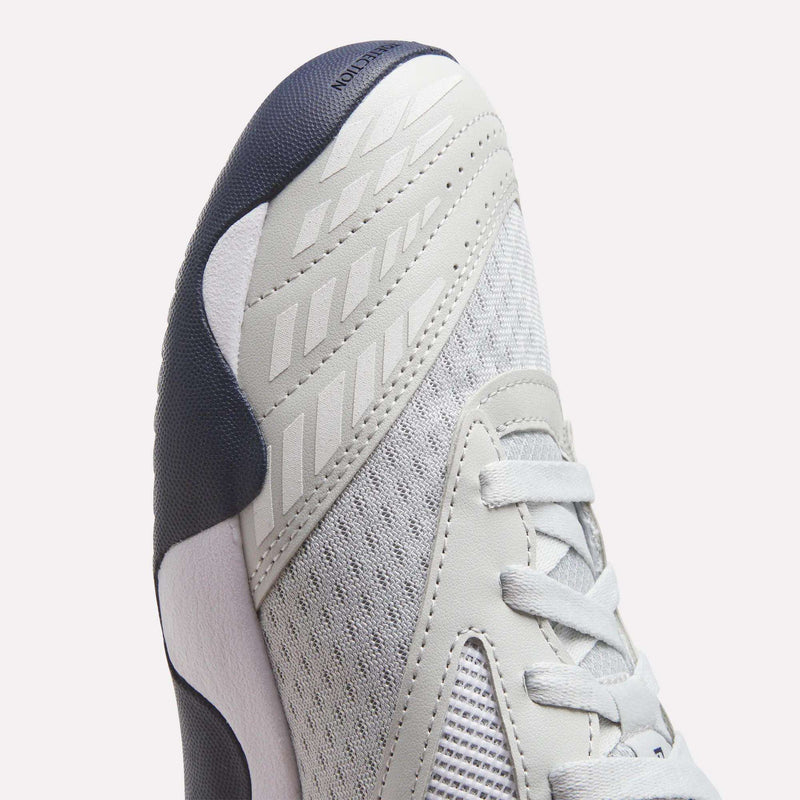 Close-up of the toe and side of a grey and white Reebok Men’s Phase Advantage Tennis Shoes, featuring a dark navy blue toe bumper and mesh upper.