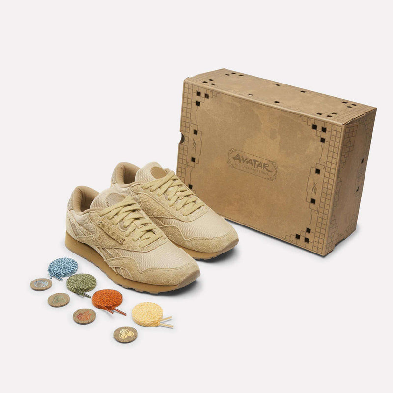 Beige Reebok x Avatar Classic Nylon shoes are displayed alongside a decorated Avatar-branded box, colorful shoelaces, and small circular tokens.