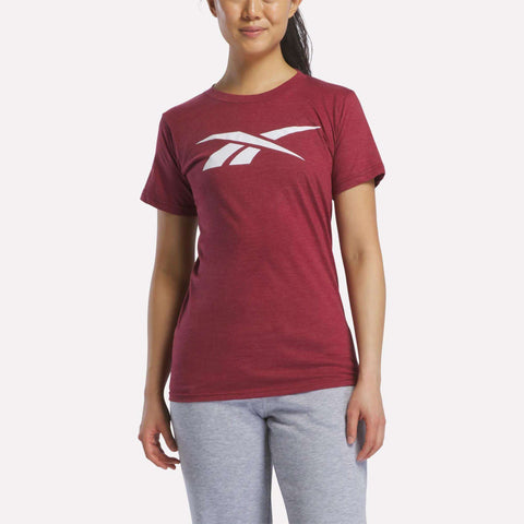 A woman wears the Reebok Women's Vector Graphic T-Shirt in maroon with a large white vector logo on the chest and light gray sweatpants, standing against a plain white background.