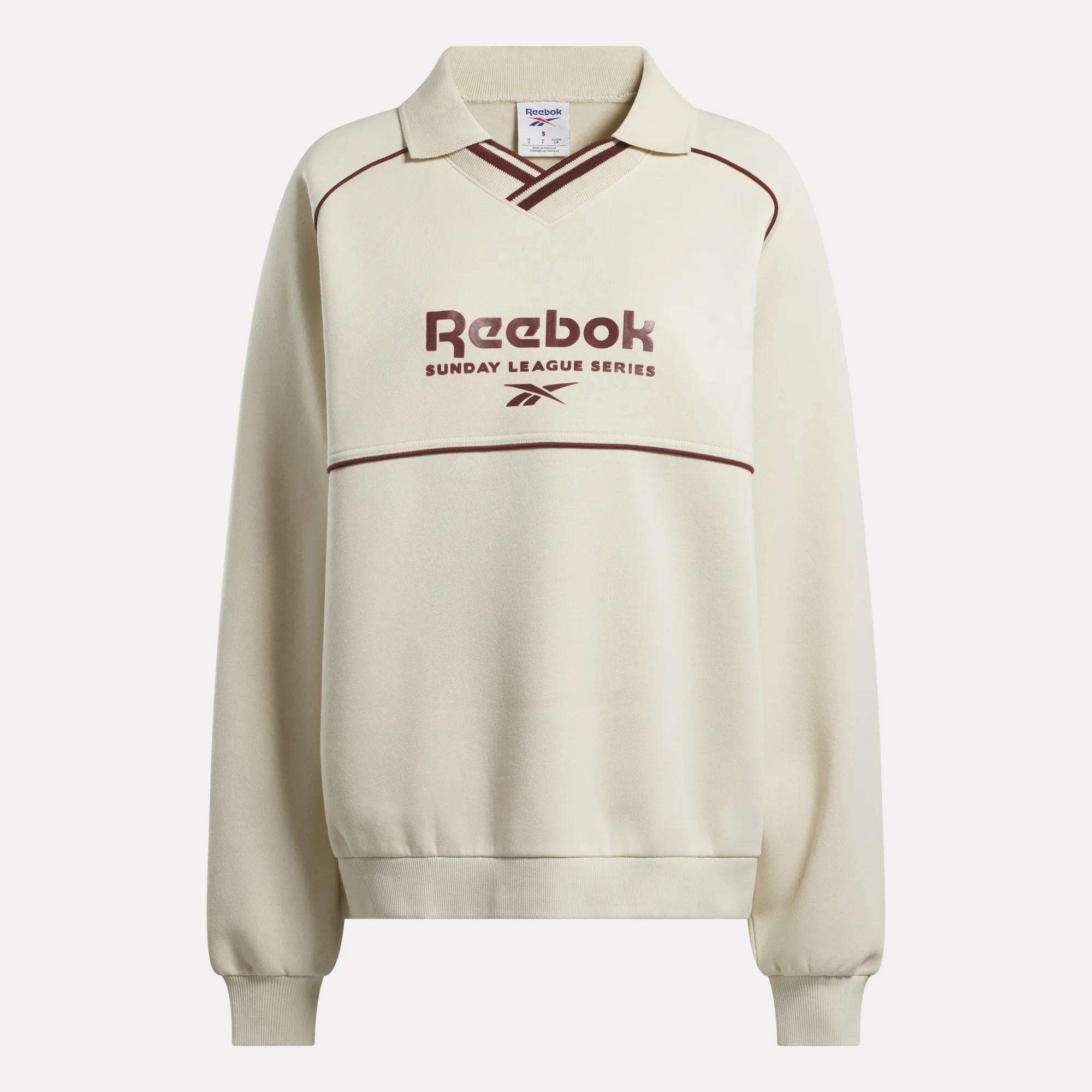 The Reebok Women's Heritage Crewneck Sweatshirt features a cream brushback fleece, collar, maroon piping, Sunday League Series text and logo on the front, plus long sleeves with ribbed cuffs and hem.