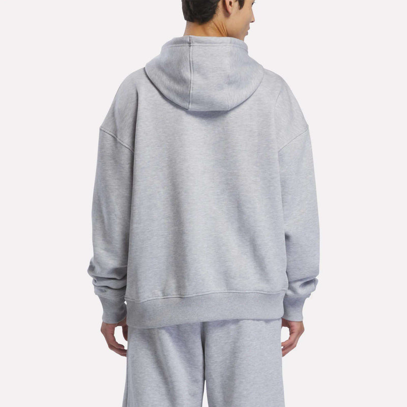 A person is shown from the back, standing against a plain white background, wearing the Reebok Men’s Starcrest Relaxed Hoodie in light gray with matching sweatpants.