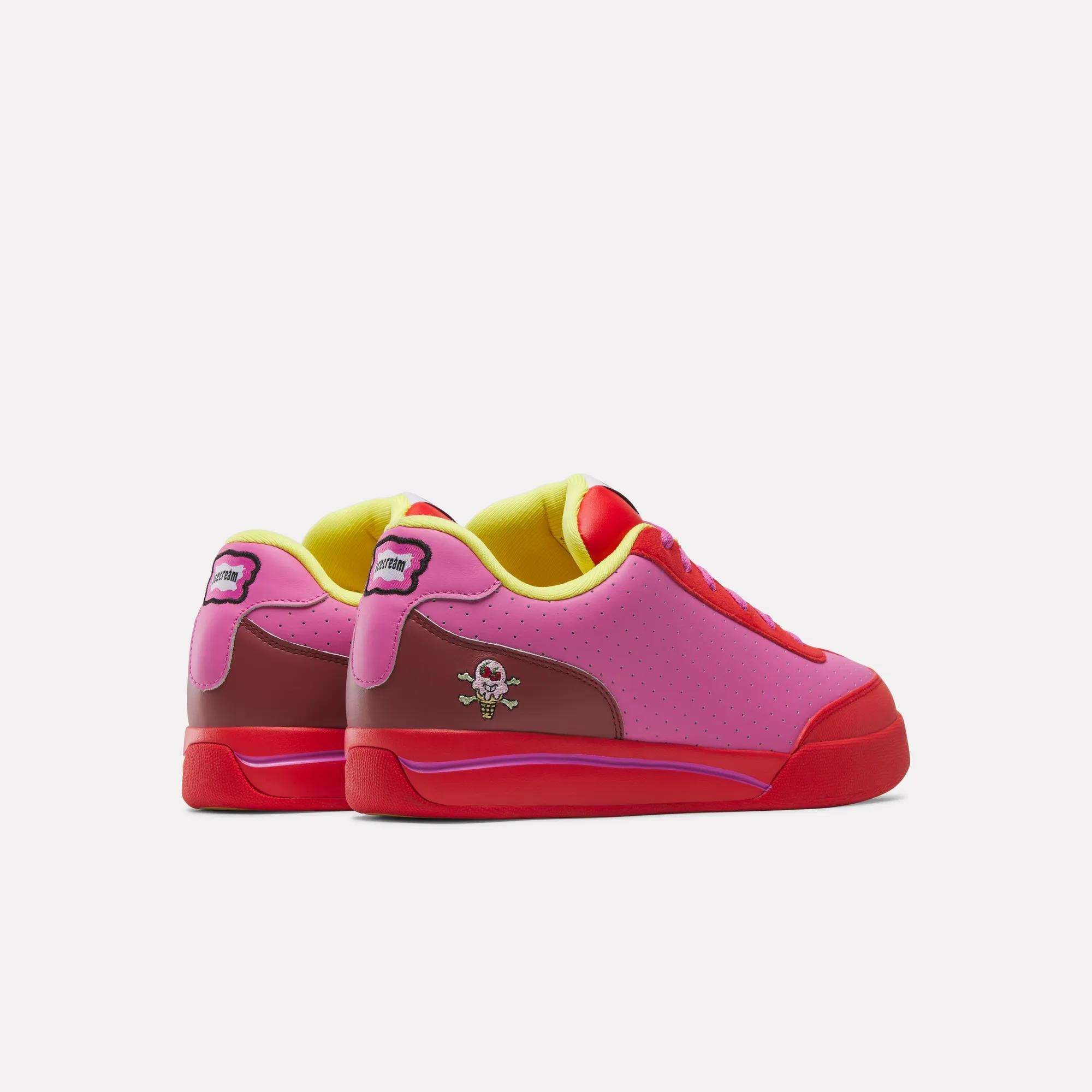 The Reebok x BBC Board Flip Skate Shoes by Reebok feature a playful street style with pink and red low-tops, yellow lining, red soles, and small cartoon character graphics on the heel and side, set against a plain white background.