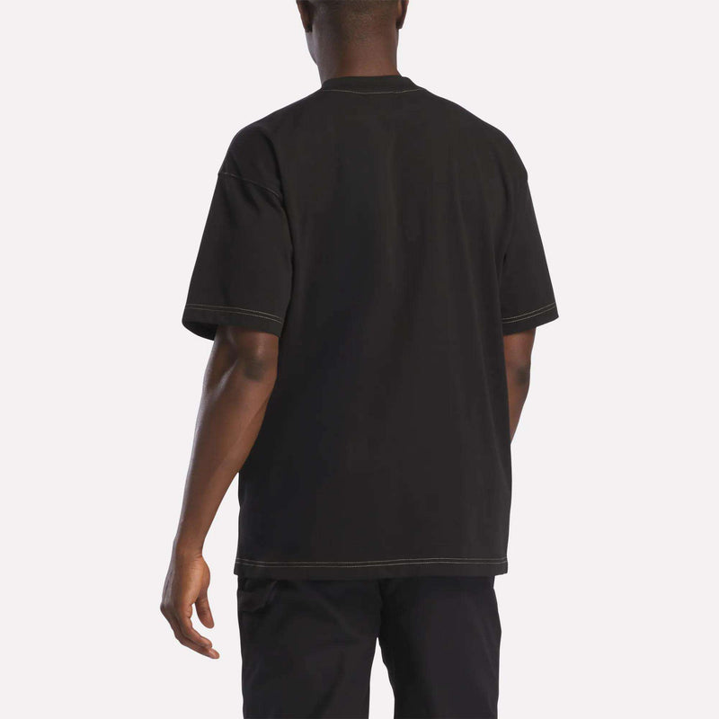 A person is shown from the back against a plain white background, wearing the Reebok Men's Big Graphic T-Shirt in black paired with black pants.