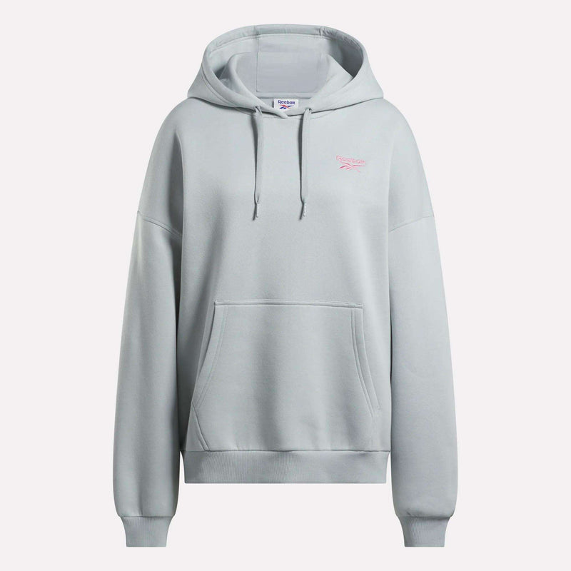 The Reebok Women's Relaxed Fleece Hoodie is an oversized light gray hoodie featuring a front pocket, drawstring hood, and a small pink Reebok logo on the left chest. It is shown against a plain white background.
