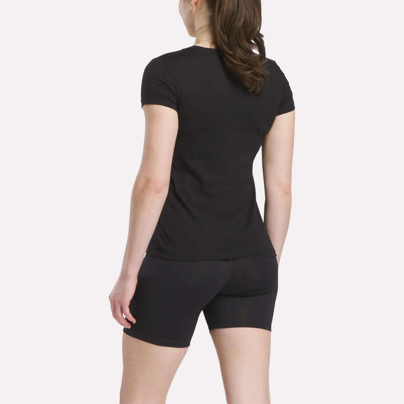 A woman stands with her back to the camera, wearing a black Reebok Women's T-Shirt and black fitted shorts, against a plain white background.