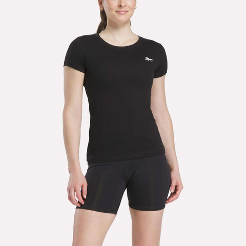 A woman wears a fitted black Women's Reebok T-Shirt with a small white logo on the chest and matching black athletic shorts, standing against a plain light background.