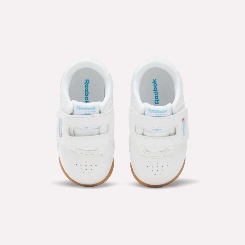 Top-down view of white Reebok Freestyle Lo Shoes for babies and toddlers, featuring two hook-and-loop straps and gum rubber soles.
