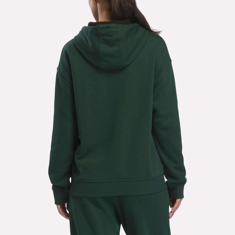 A person wearing the Reebok Women’s French Terry Lawn Club Hoodie in dark green, along with matching pants, stands facing away to display the back of the outfit against a plain white background.