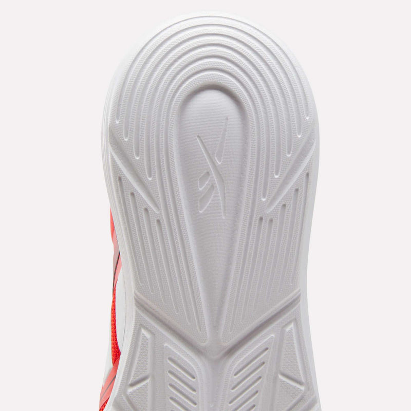 Close-up of the white outsole of Reebok Rush Runner 6.0 Running Shoes for big kids, showing textured grooves, geometric traction patterns, and a small logo. Red mesh accents and an EVA midsole are partly visible on the side.