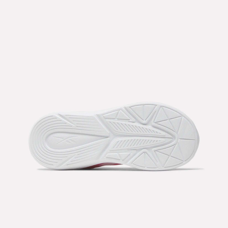 The image shows the bottom view of a white Reebok Rush Runner 6.0 Elastic Lace Top Strap Running Shoe sole for little kids, featuring a textured pattern with grooves, lines, and geometric shapes on a plain light background.